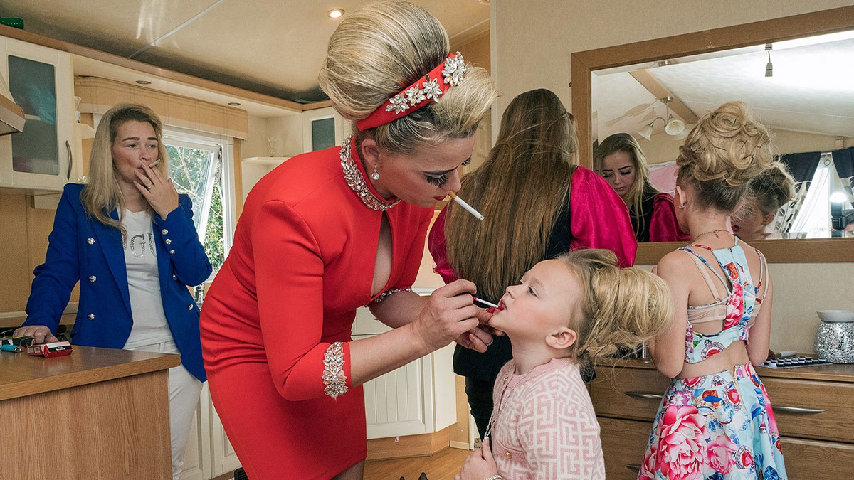 Woman applying lipstick to a child while smoking indoors, capturing life on the margins of modern Ireland.