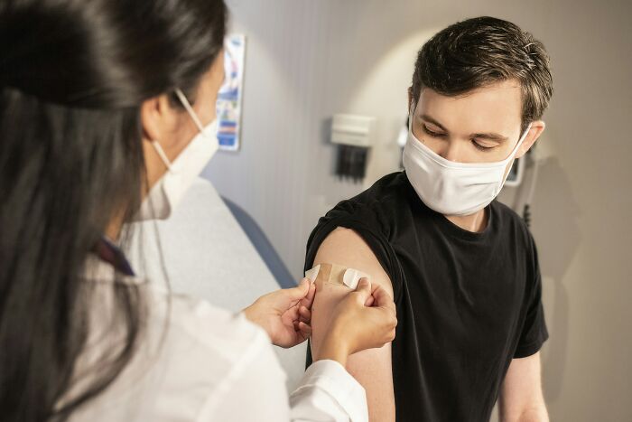 Healthcare professional applying a bandage on a young man's arm after vaccination, addressing debunked lies people believe.