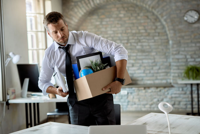 Man in white shirt and loosened tie carrying a box of office items after tracking missing equipment for months. Man in white shirt and loosened tie carrying a box of office items after tracking missing equipment for months.
