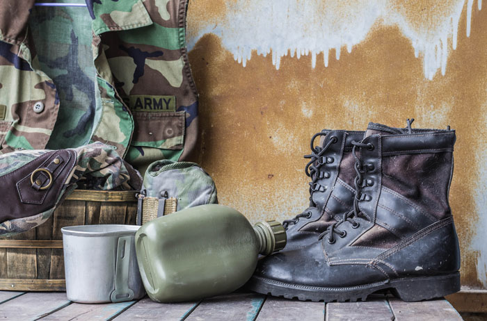 Worn military boots, canteen, and army uniform displayed on wooden floor representing soldier tracking missing equipment.