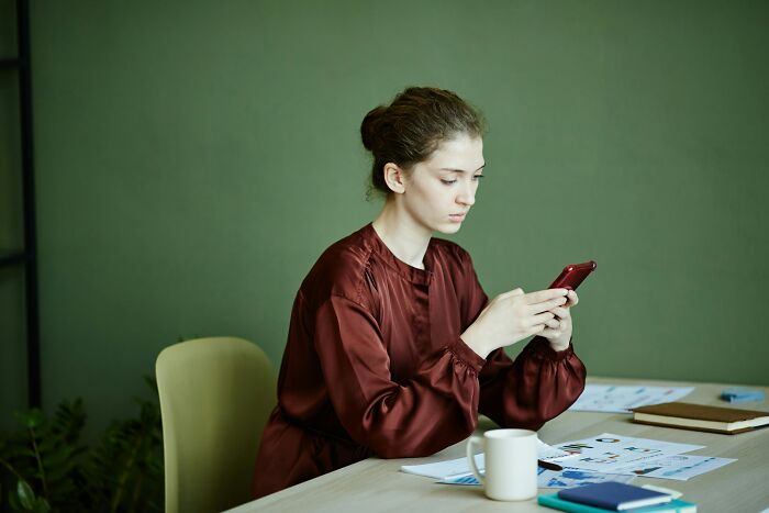 Young woman refusing to be the go-to nanny on a trip, focused on her phone while sitting at a desk with papers. Young woman refusing to be the go-to nanny on a trip, focused on her phone while sitting at a desk with papers.