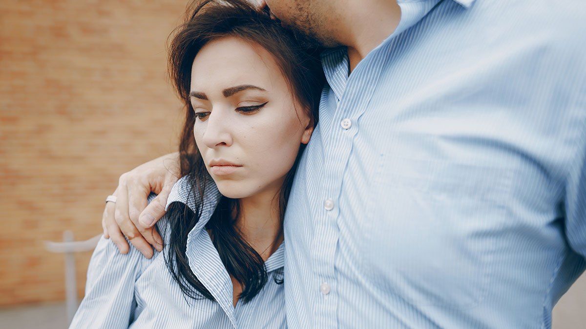 Woman refusing to be go-to nanny on couples trip, showing frustration while being comforted by a man in blue shirts.