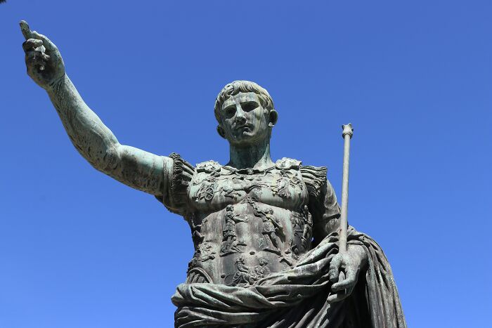 Bronze statue of a Roman emperor with raised arm against a clear blue sky, symbolizing crazy but real historical events.