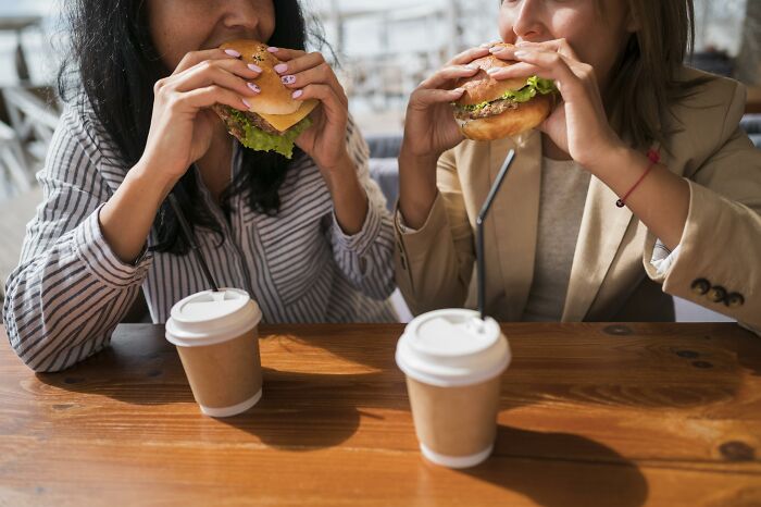 Two people eating burgers and drinking coffee, illustrating McDonald's employees sharing bizarre experiences.