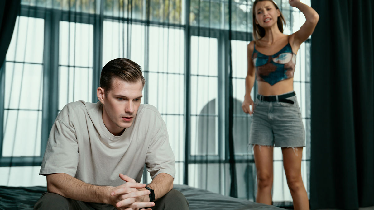 Young couple in a heated argument on first day of vacation, man sitting with worry and woman standing upset indoors.