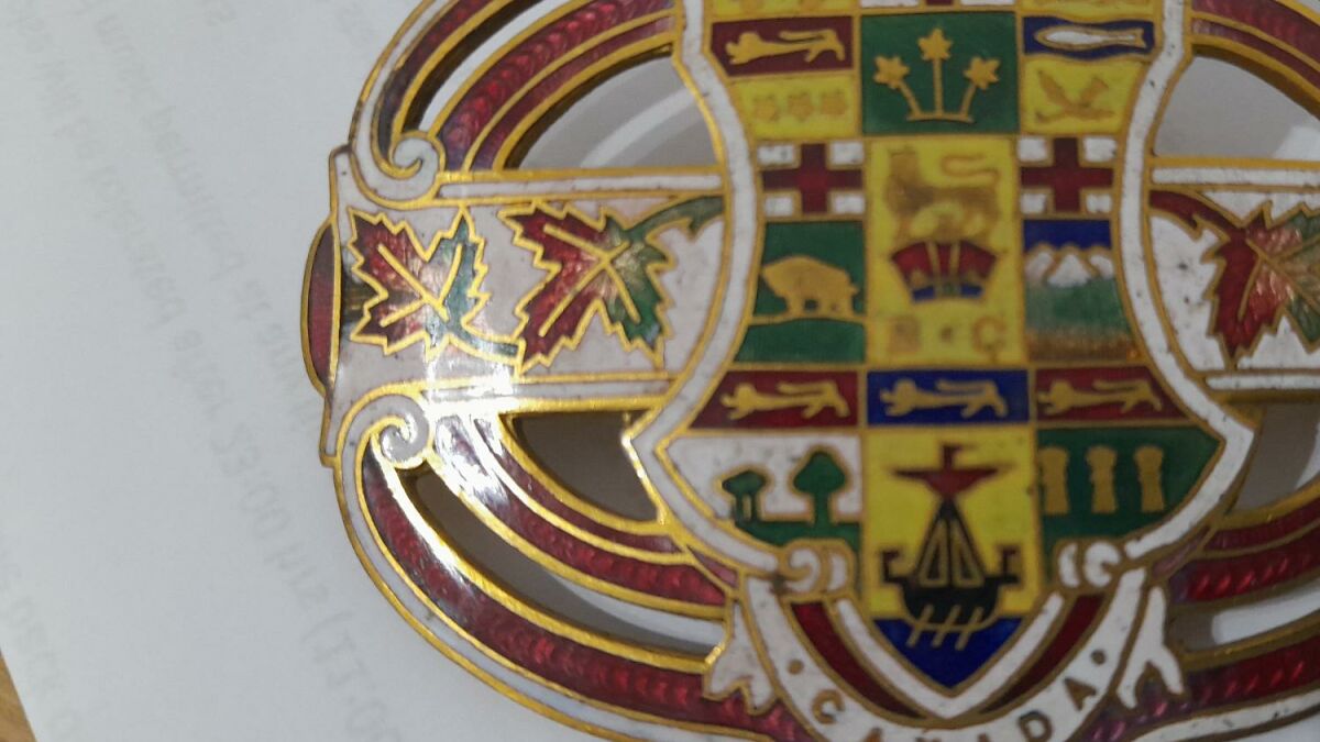 Close-up of an ornate Canada brooch featuring colorful enamel with maple leaves and a detailed coat of arms design.