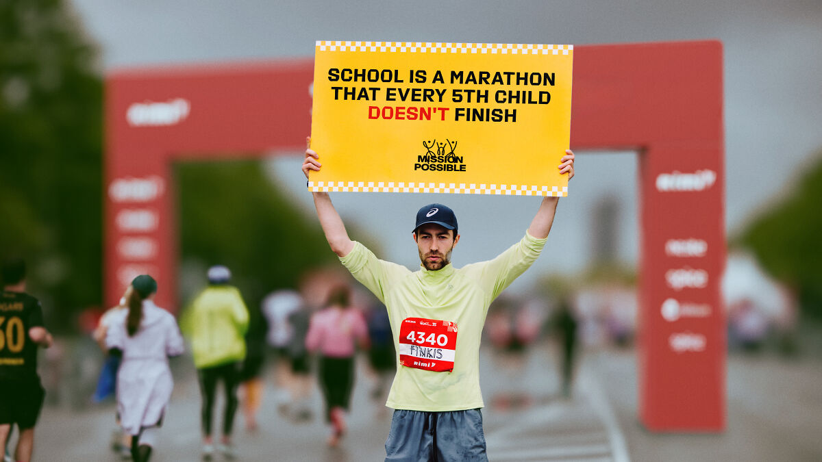 Latvian rapper holding a sign about education dropping out while standing near a marathon finish line.