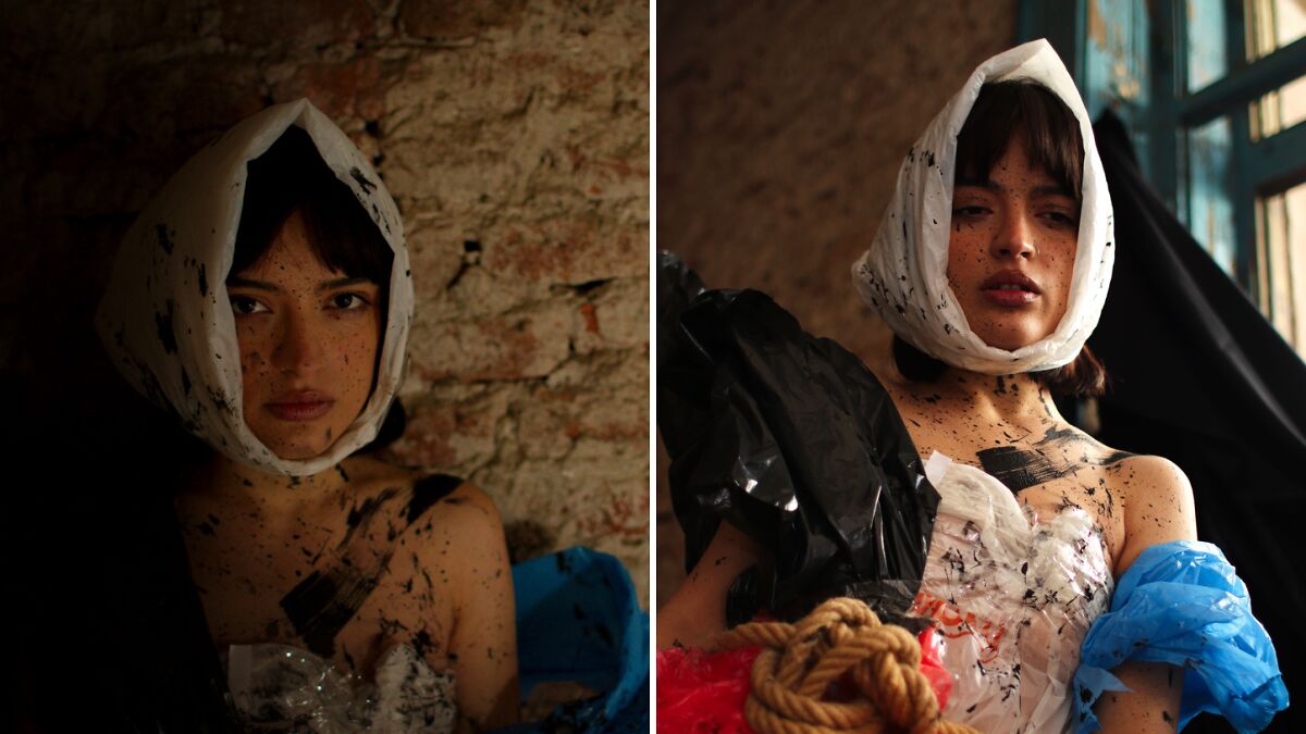 Female model with paint splatters wearing creative plastic and fabric fashion in a dimly lit fashion photography project setting.