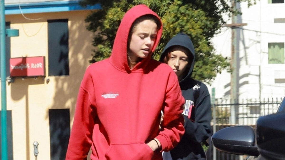 Shiloh Jolie-Pitt in a red hoodie with a companion wearing a black hoodie, fueling romance rumors during a public outing.