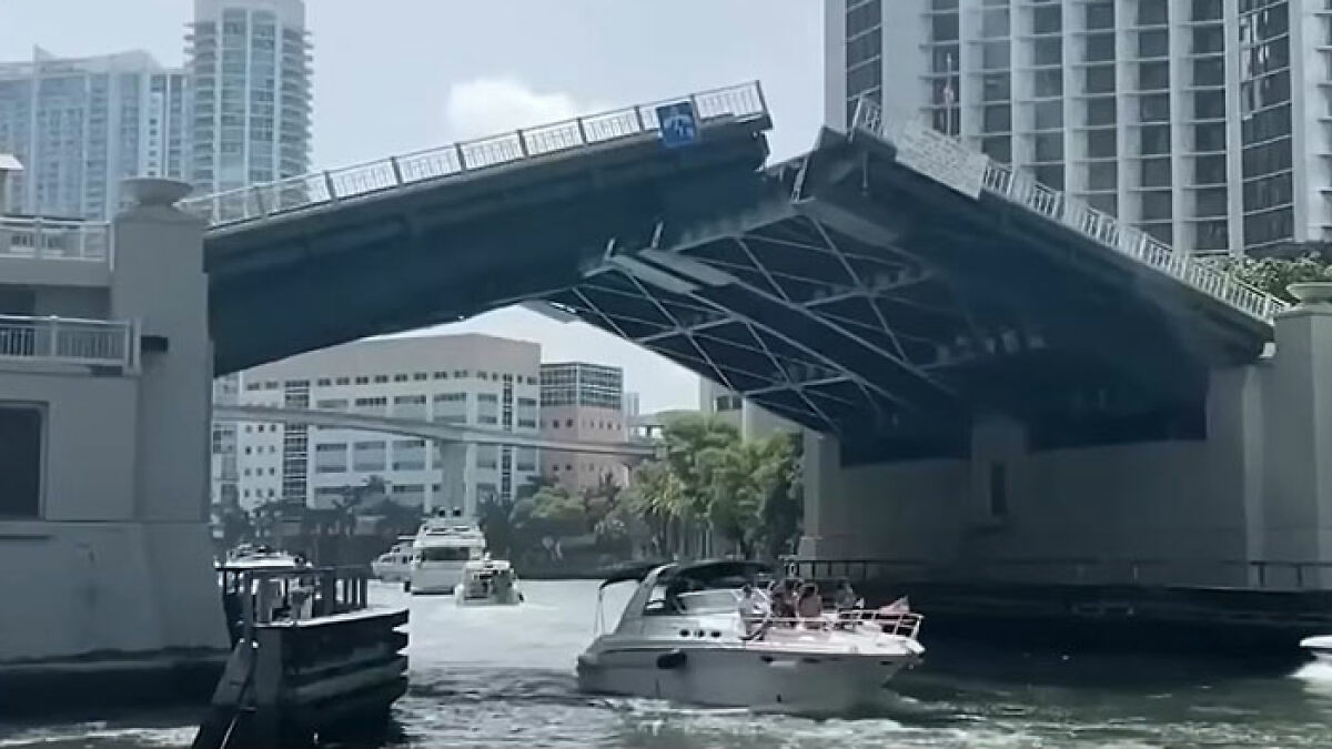 Drawbridge rising over a waterway with boats passing underneath near urban high-rise buildings.