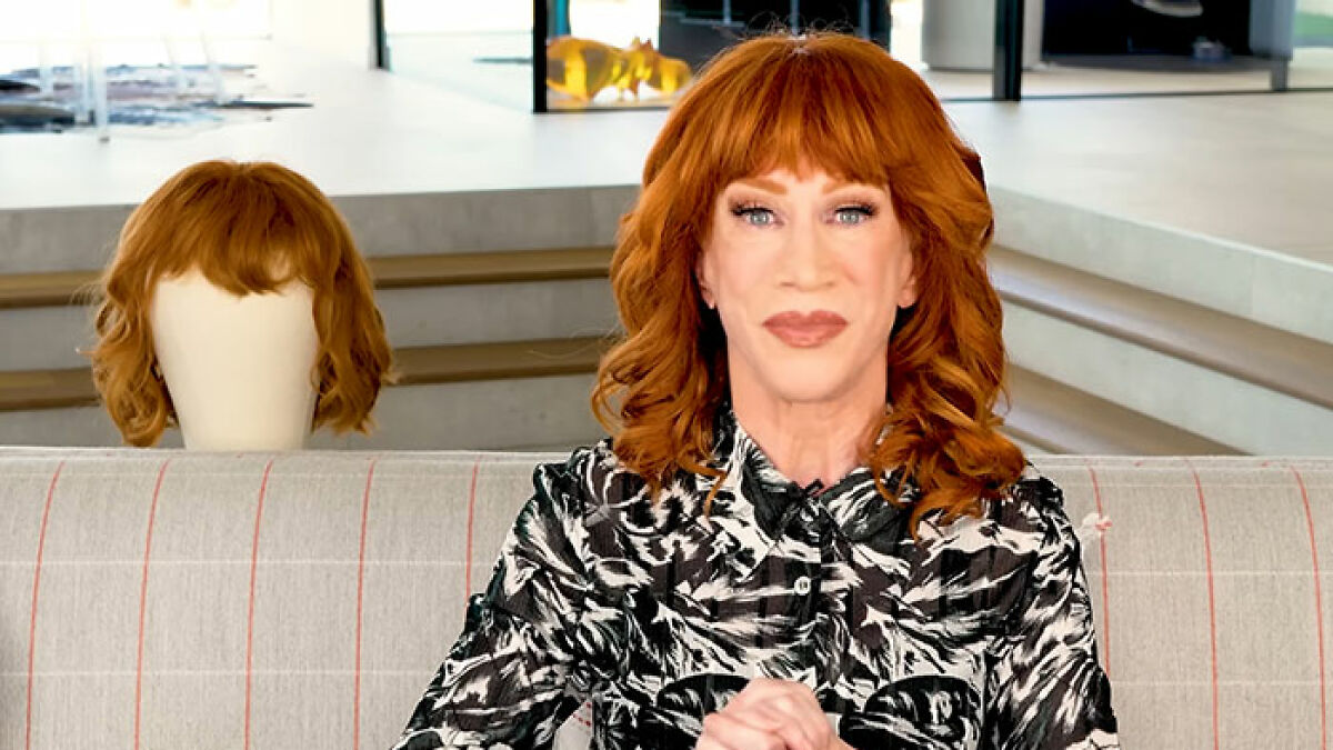 Kathy Griffin with red hair sitting on a couch indoors alongside a wig, showcasing natural transformation meme moment.