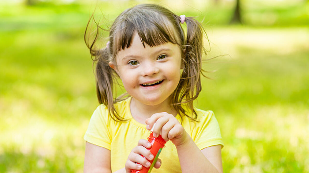 Smiling young girl with Down syndrome playing outside in yellow shirt, representing gene editing scientific breakthrough.