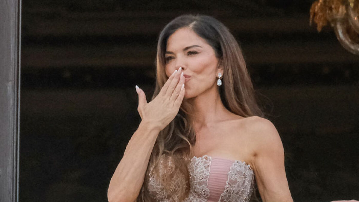 Lauren Su00e1nchez in an elegant strapless dress blowing a kiss with long hair and teardrop earrings against a dark background