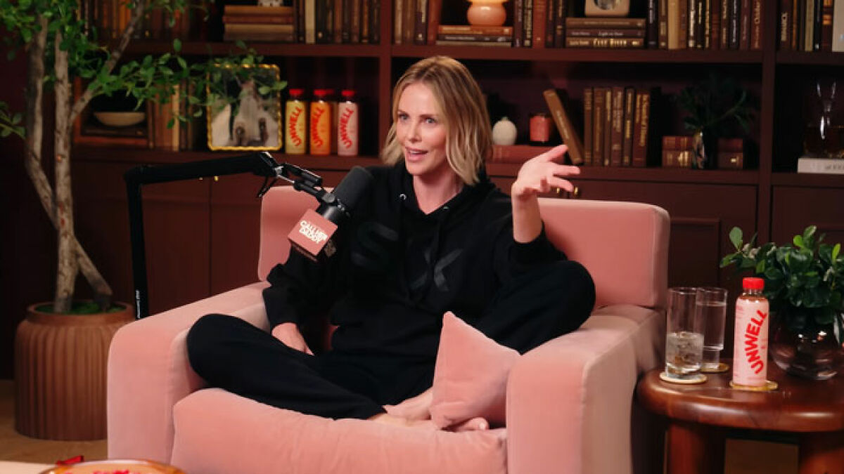 Charlize Theron sitting in a podcast studio, speaking into a microphone during a casual interview discussion.