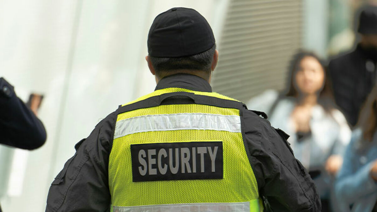 Security officer in a high-visibility vest monitoring passengers after a flight scare causing emergency landing.
