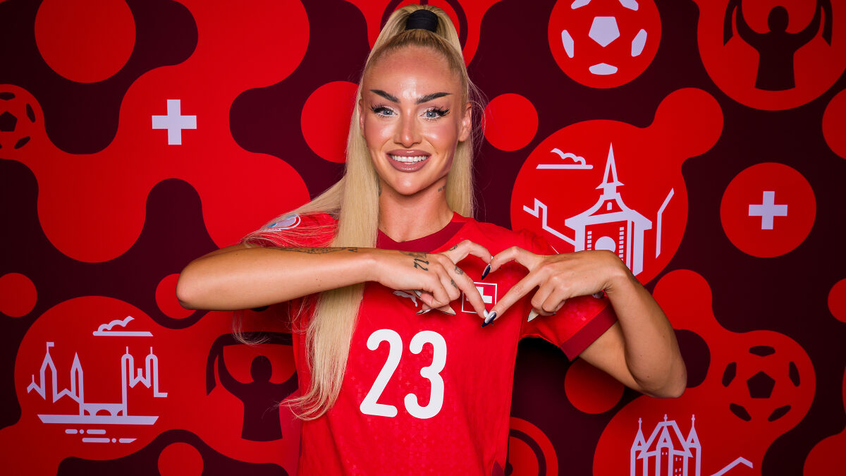 World's prettiest footballer in red jersey making heart shape with hands against vibrant red sports backdrop.