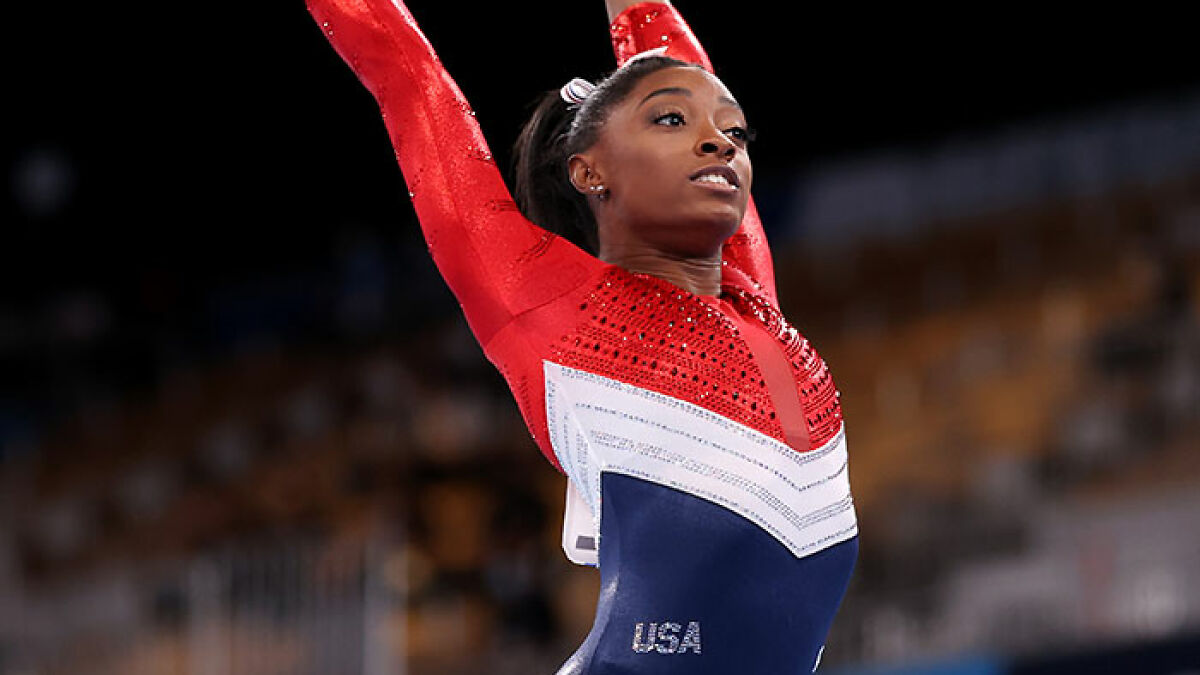 Simone Biles performing gymnastics in a red, white, and blue USA leotard during a competition.