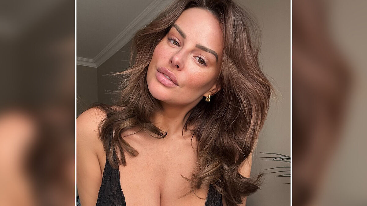 Rhian Sugden posing indoors with styled hair and natural makeup amid $13K plastic surgery fan backlash controversy.