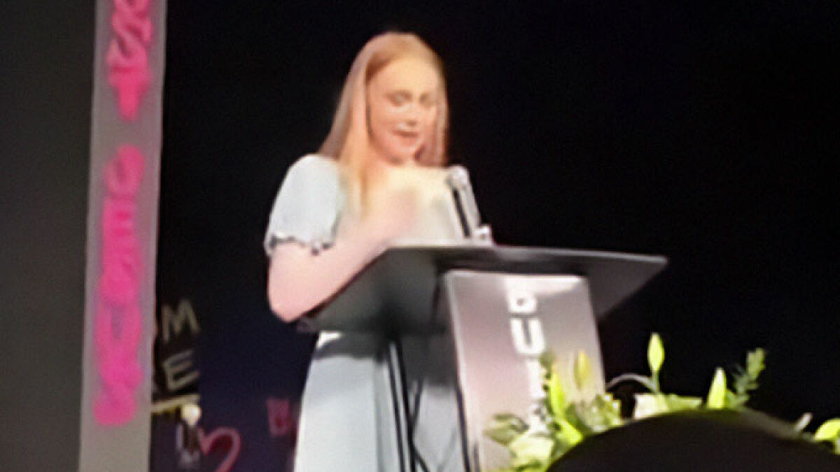 Teen girl giving a chilling eulogy at a podium, causing police to suspect she slayed her own parents in their sleep.