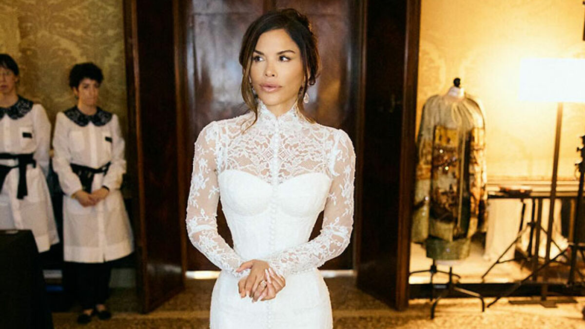 Lauren Sanchez in a white lace wedding dress, posing indoors with staff members and ornate decor in the background.