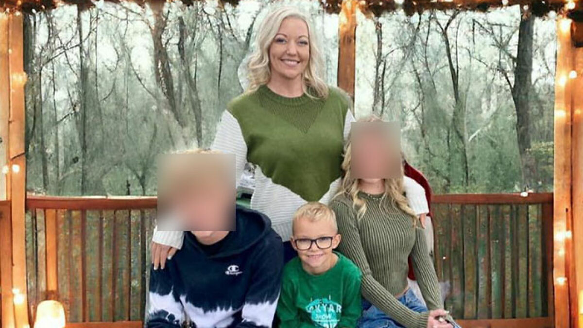 Family portrait with a teen and young children outdoors on a wooden deck surrounded by trees and string lights.
