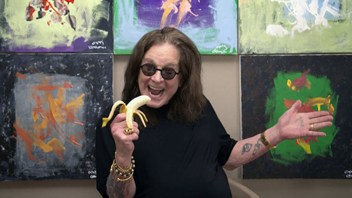 Ozzy Osbourne holding a banana, surrounded by abstract art paintings created with chimps for charity.