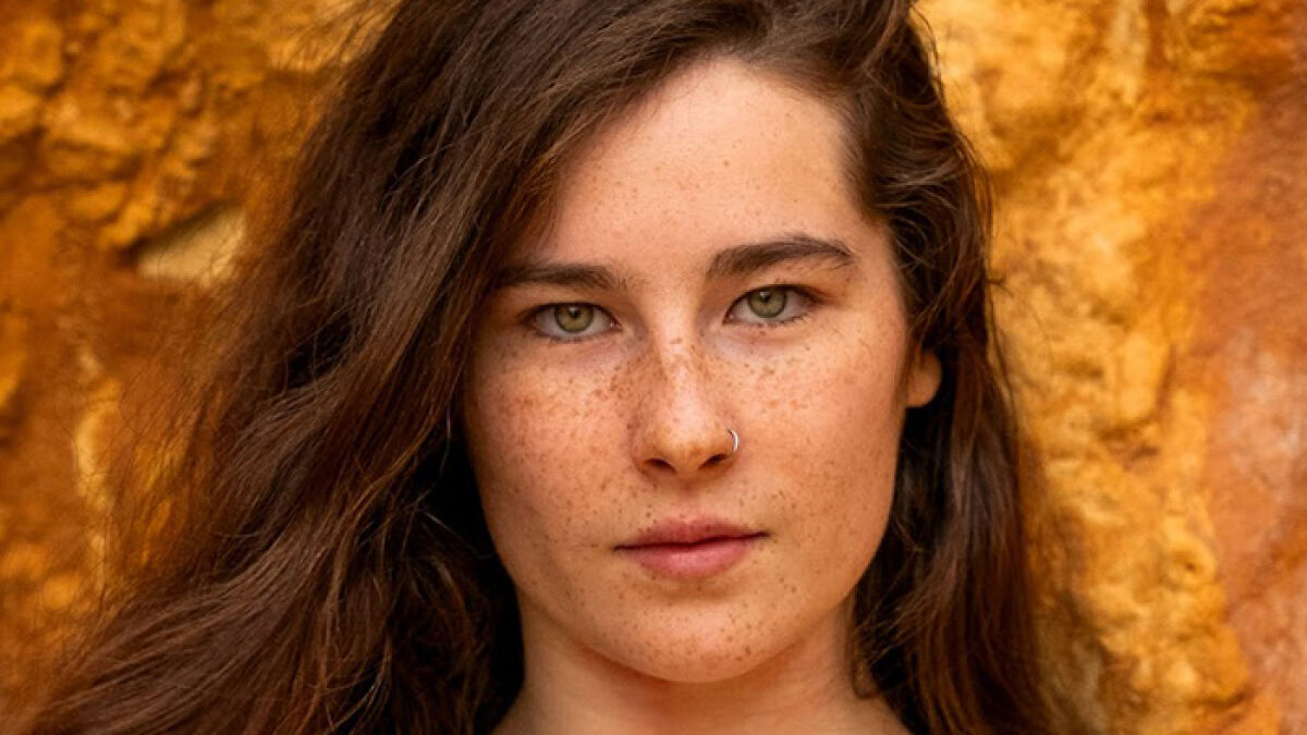 Young Gen Z woman with natural look and freckles, standing against a warm textured background, embracing body positivity.