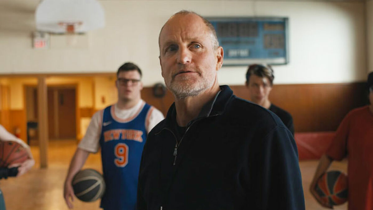 Woody Harrelson in a gym with basketball players, focusing on his intense expression and athletic setting.