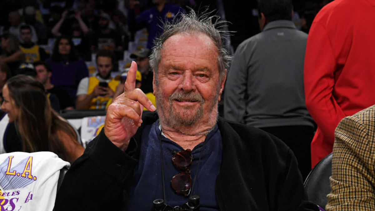 Jack Nicholson at a basketball game, smiling and gesturing, amidst fans concerned about his health and frail appearance.