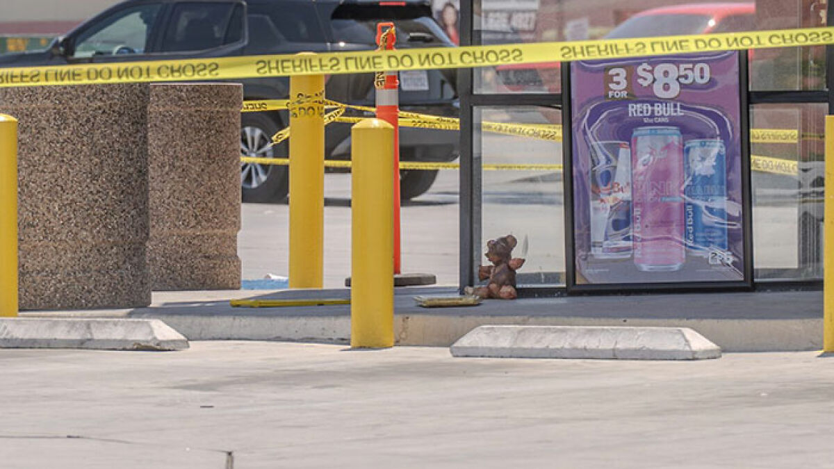 Teddy bear covered in apparent human remains sitting outside convenience store with police tape surrounding the area.