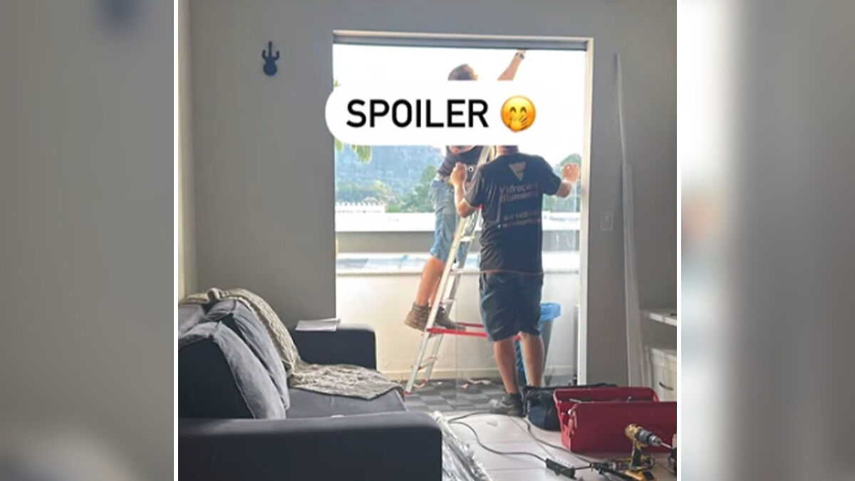 Two workers setting up equipment on a balcony while a living room sofa and tools are visible inside the apartment.