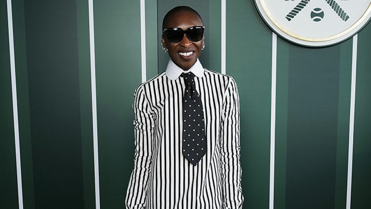 Celebrity at Wimbledon 2025 in a black and white striped shirt with polka dot tie, wearing sunglasses and smiling.