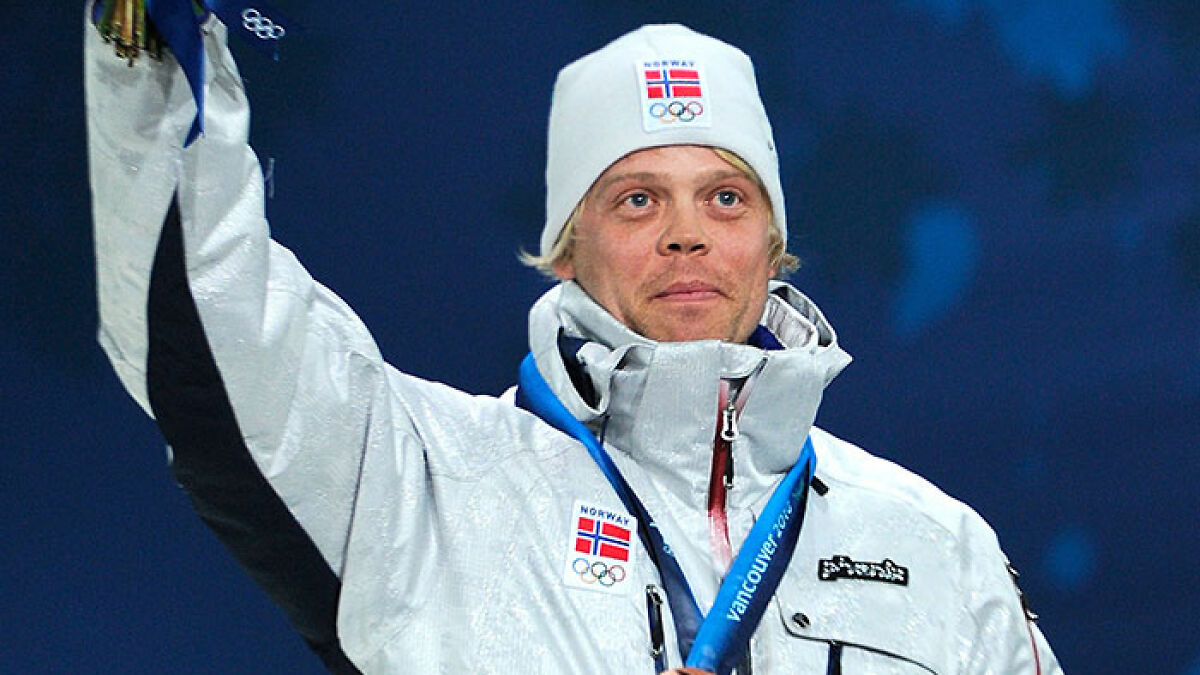 Olympic medalist skier wearing Norway gear and a medal, raising hand during award ceremony in winter sports event.