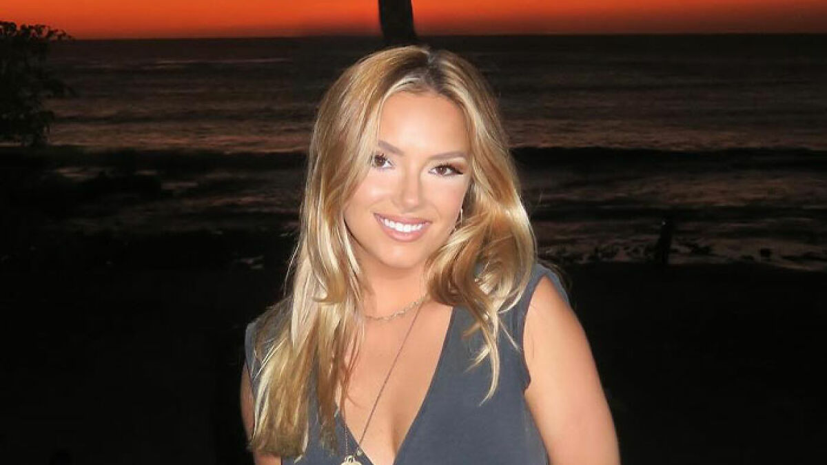 Young woman smiling at sunset by the beach, related to Coldplay fan who exposed cheating CEO at concert.