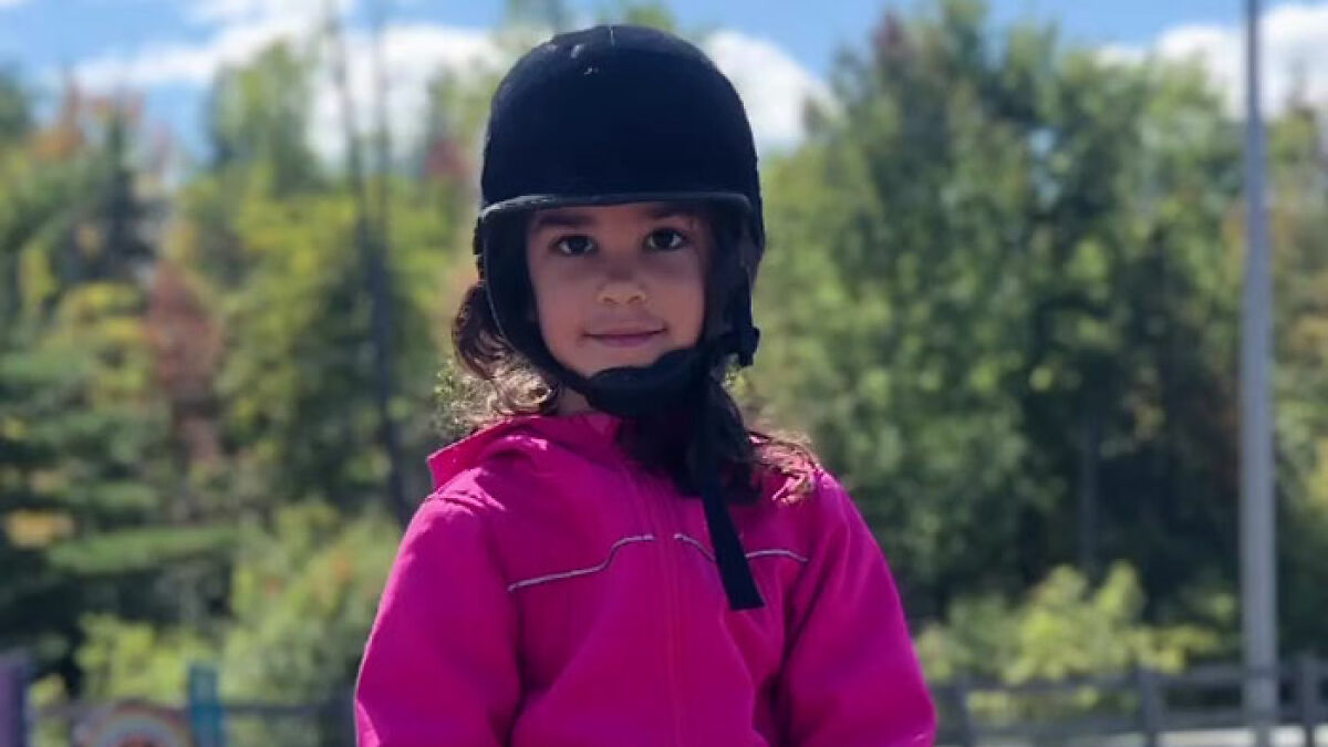 Young girl wearing a black helmet and pink jacket outdoors with police investigating inconsistencies in missing child report