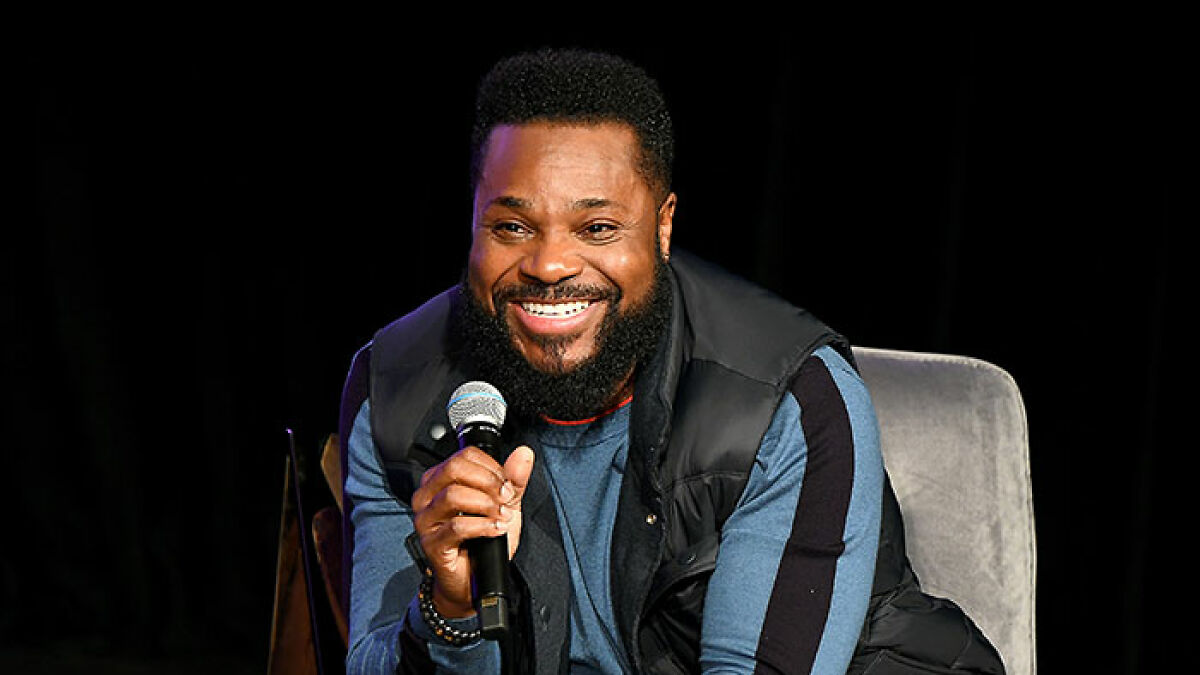 Man speaking into a microphone and smiling during a public event, related to Bill Cosby and Malcolm-Jamal Warner news.