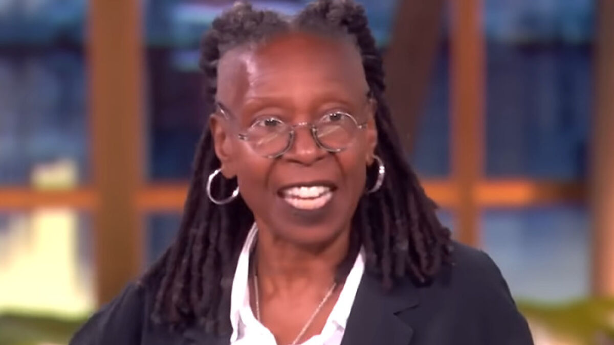 Whoopi Goldberg speaking on a TV show, wearing glasses, hoop earrings, and a black blazer over a white shirt.