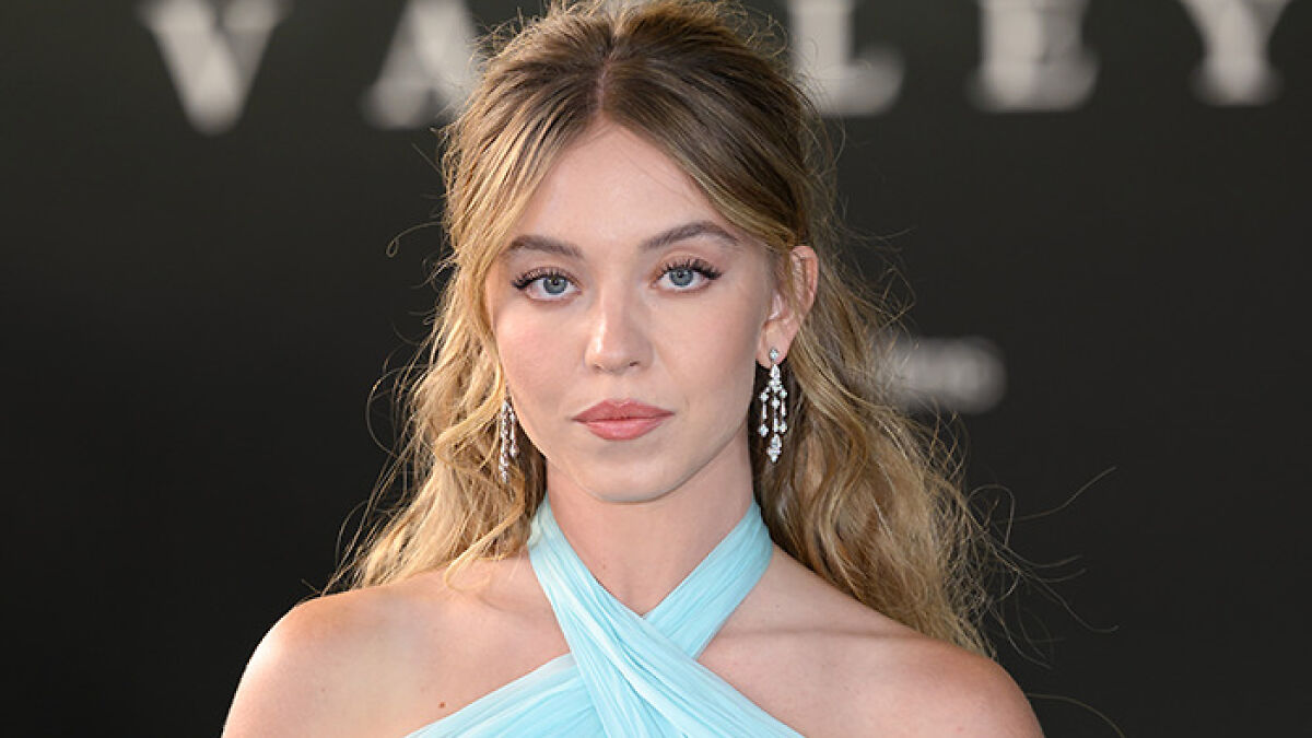 Sydney Sweeney at a red carpet event with elegant earrings and a light blue halter dress, showcasing her dramatic transformation.