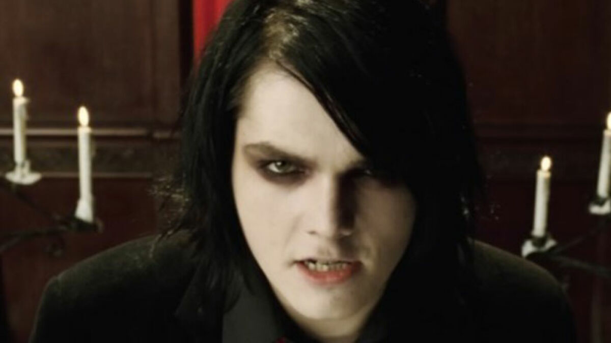 Emo musician with dark hair and makeup performing in a dimly lit setting with candles in the background.