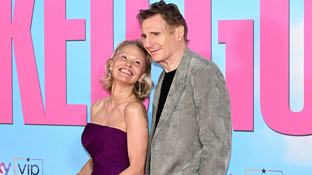 Pamela Anderson and Liam Neeson smiling and posing closely on the red carpet at a movie premiere event.