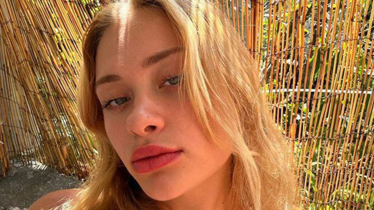 Young female model with blonde hair posing outdoors near bamboo fence, related to broken limbs and spine incident in Dubai.