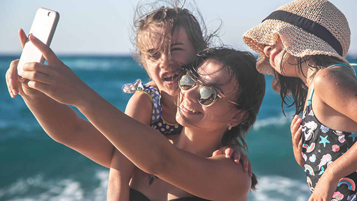 Momfluencer taking a staged beach day selfie with daughters by the ocean to gain online fame and followers.