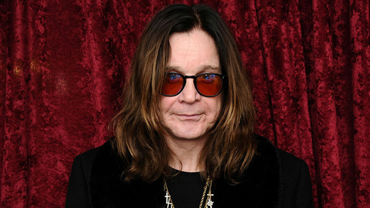 Rock star with long hair and red-tinted glasses against red curtain backdrop, representing stars lost this year.