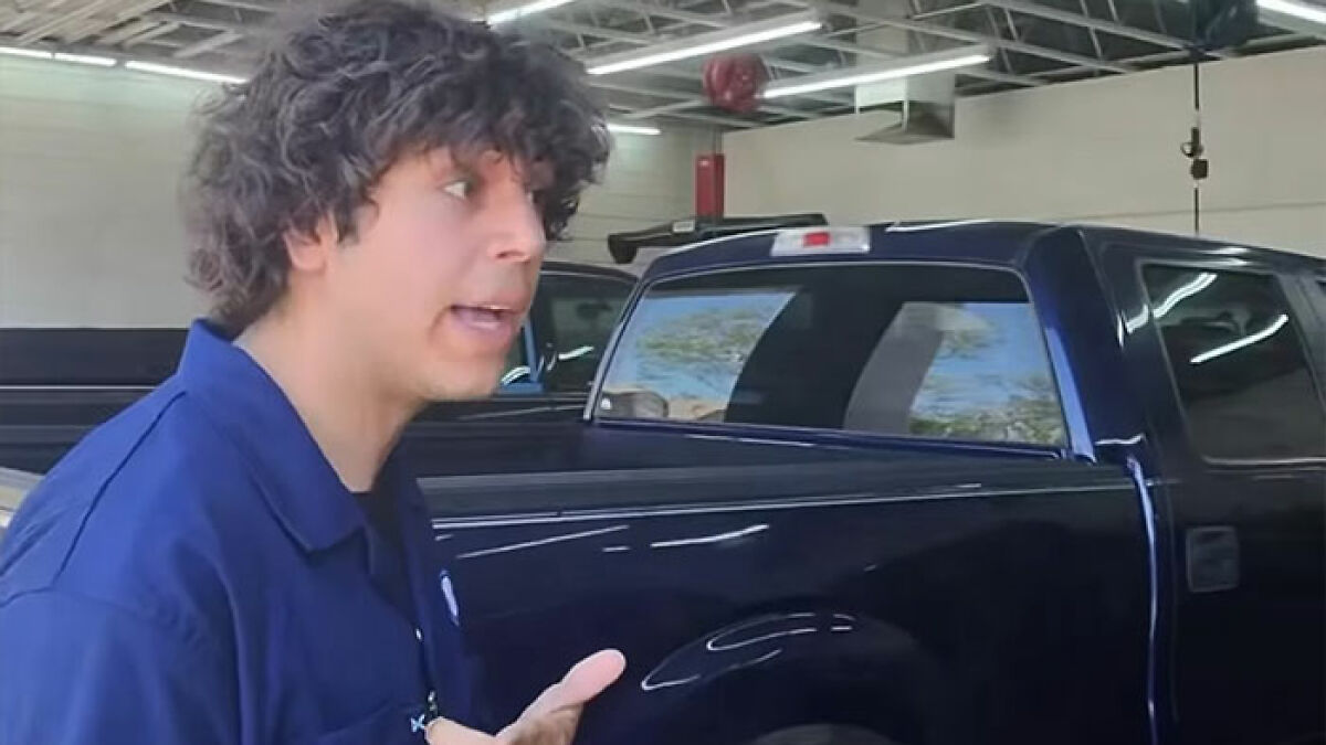 Young man in a blue shirt talking beside a black pickup truck inside a garage, related to viral TikToker prank arrest.