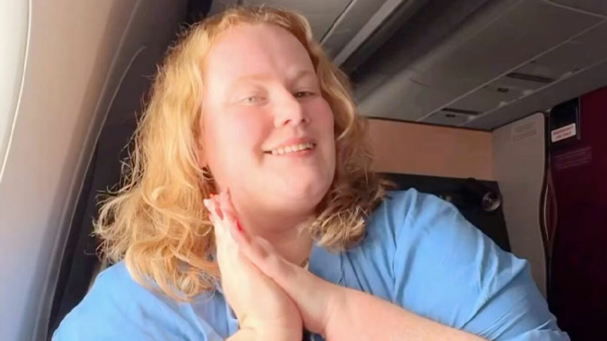 Plus-size traveler smiling on airplane, sharing reasons for not booking two airline seats despite criticism.
