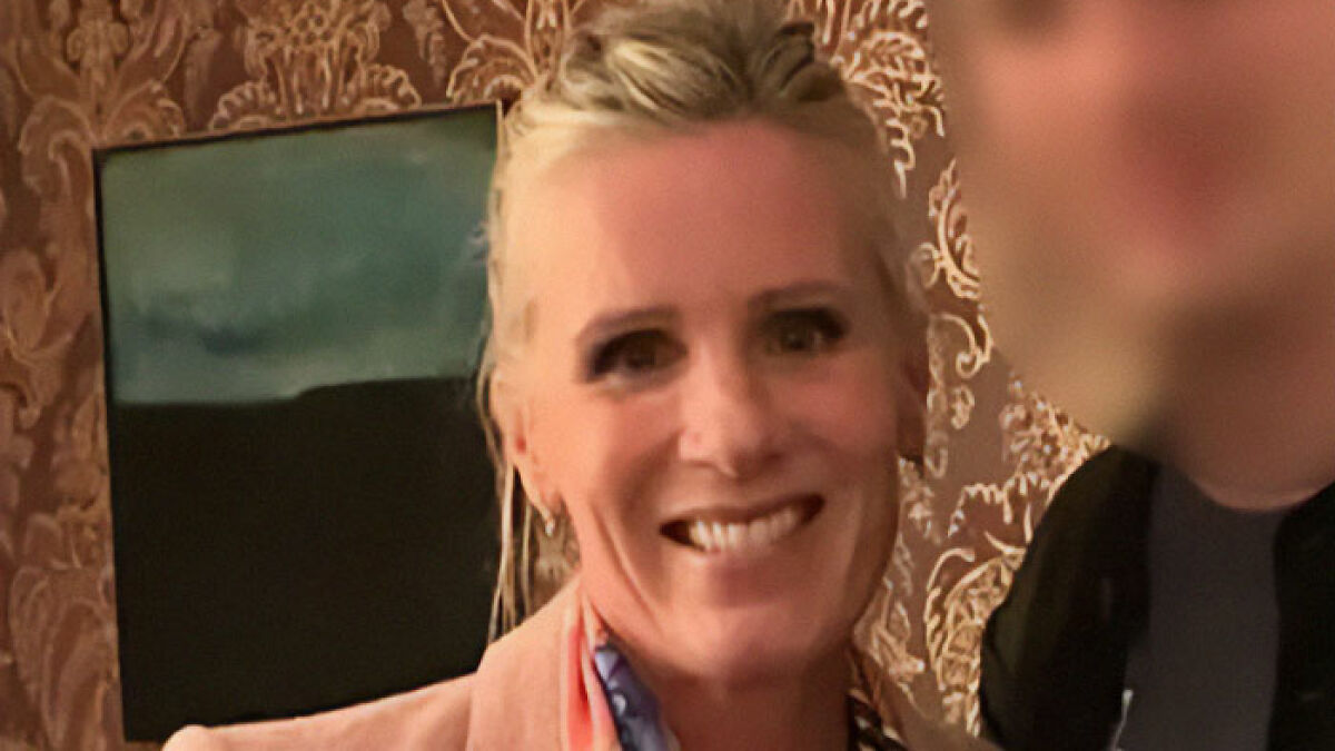 Coldplay HR executive smiling indoors with blurred person beside her and decorative wallpaper background.