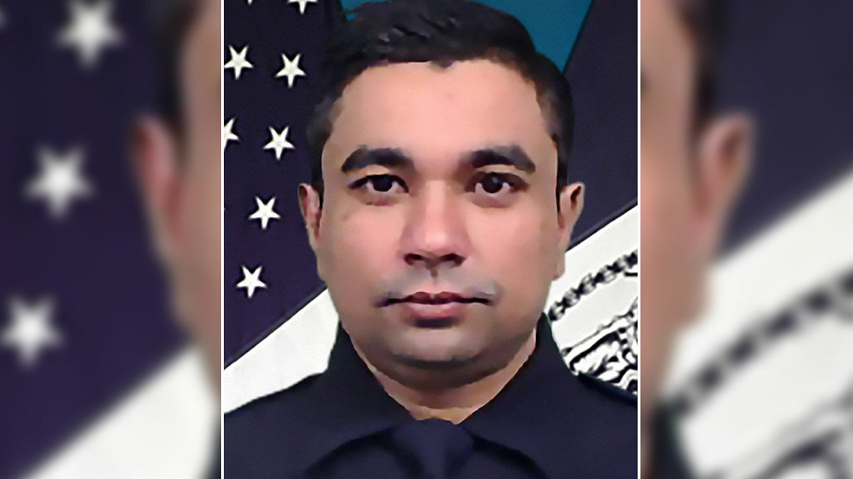 NYPD cop in uniform with an American flag backdrop, honoring officer fatally shot while protecting others.