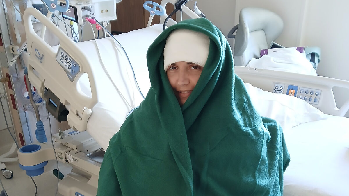 Paralyzed woman wrapped in green blanket in hospital bed, showcasing Elon Musk Neuralink brain chip technology.
