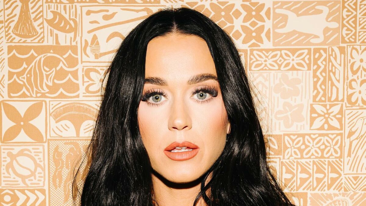 Close-up of Katy Perry with dark hair against patterned background related to Katy Perry and Justin Trudeau romance rumors.