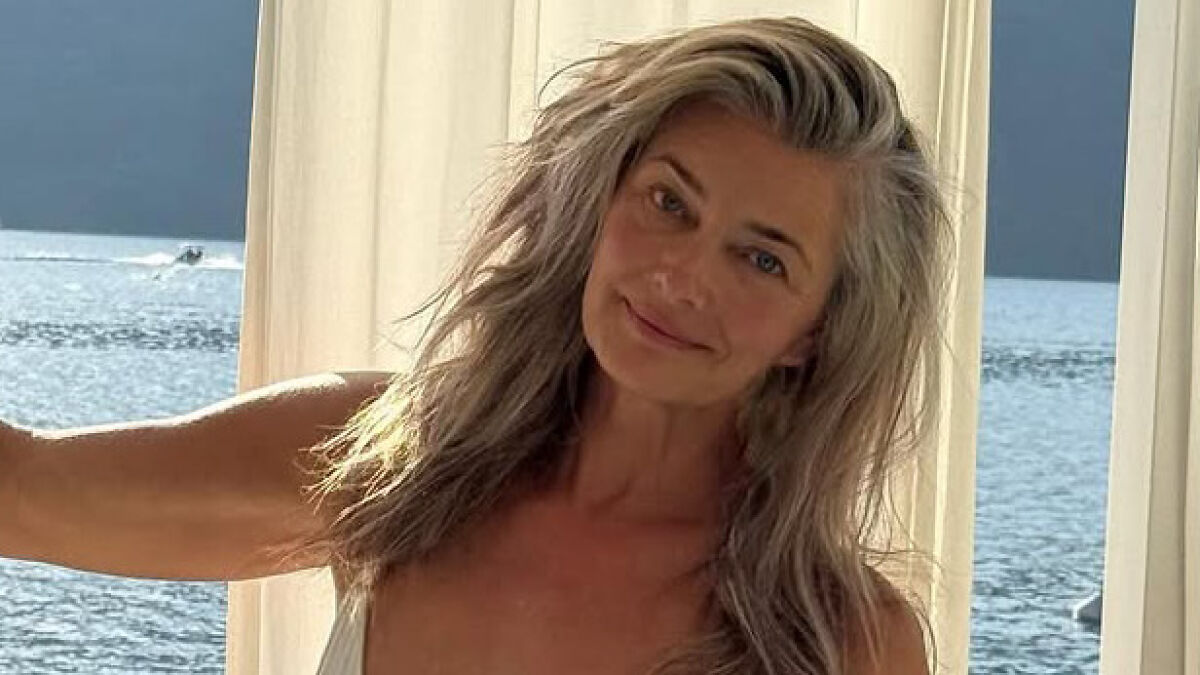Supermodel at 60 with natural look and gray hair, smiling by the sea without filters, embracing aging gracefully.